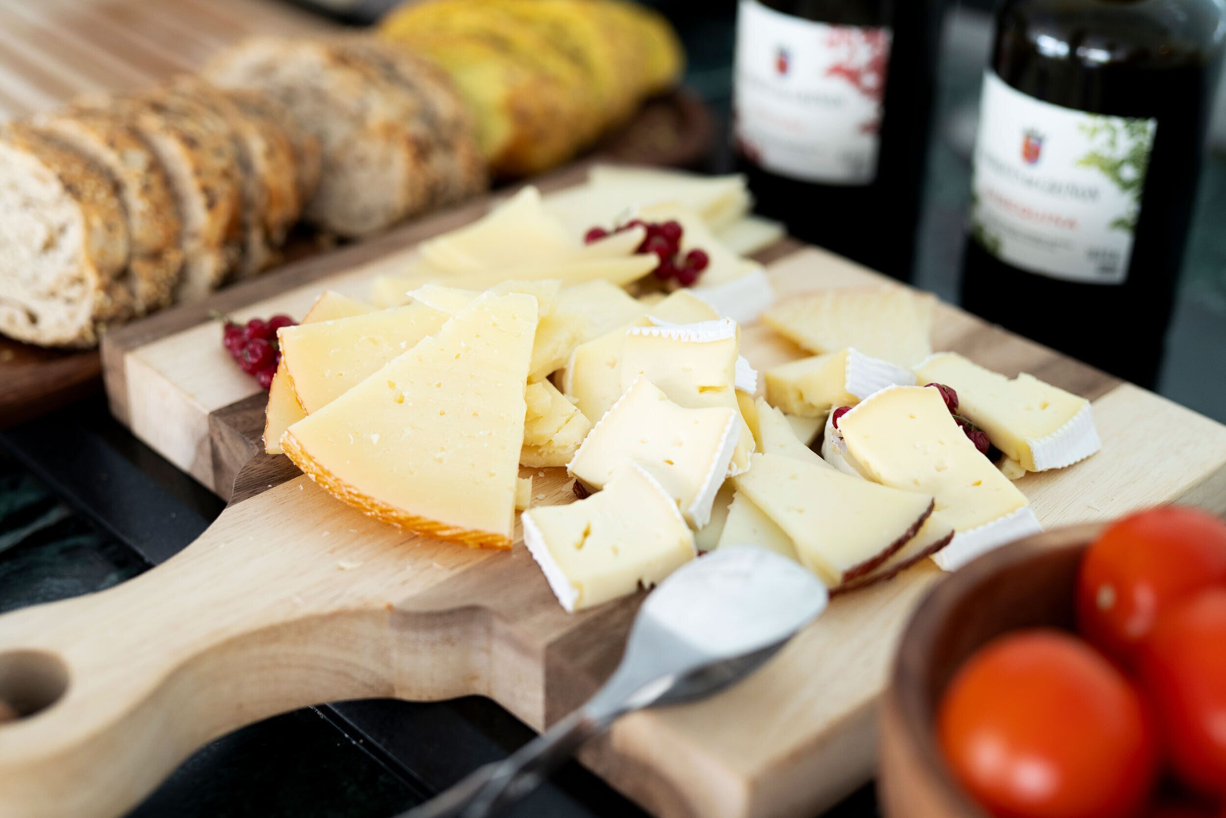 Una tabla de madera con queso, pan y una botella de vino.