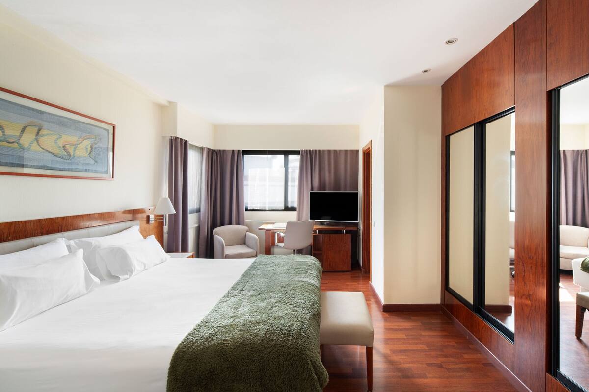 A hotel room with a bed, desk, chair, TV, and a large mirror.