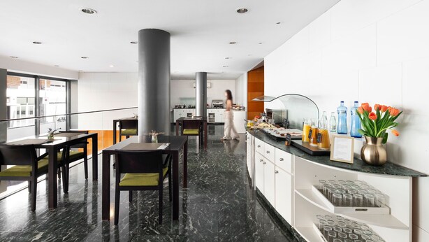 A modern hotel lobby with a dining area, a reception desk, and a large pillar. - Bohemian Entenza (Barcelona)