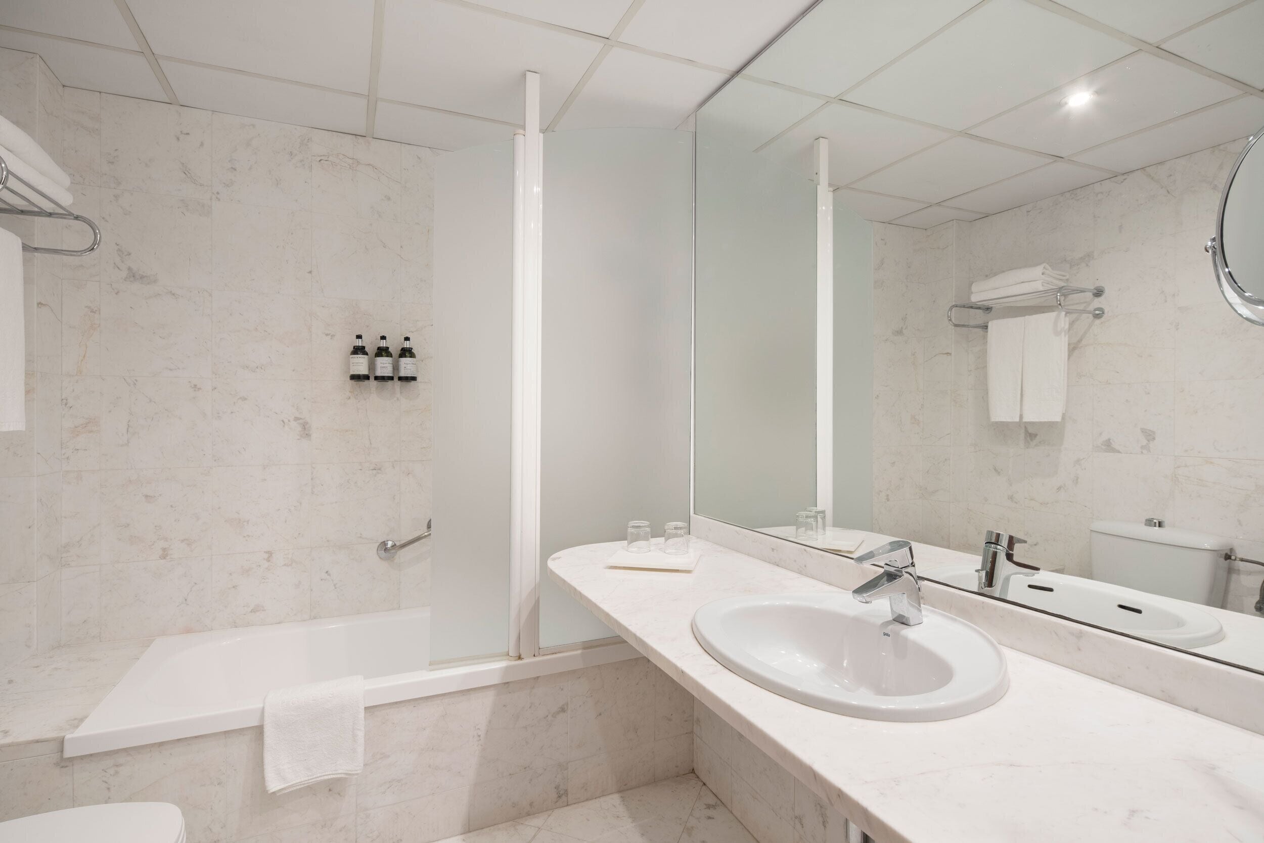A modern bathroom with a bathtub, a sink, a mirror, and a toilet.