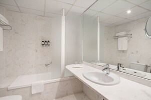 A modern bathroom with a bathtub, a sink, a mirror, and a toilet.