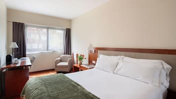 A hotel room with a bed, desk, chair, lamp, and window.