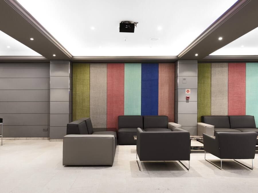 Un espace de détente moderne avec un sol gris, des canapés noirs et un mur rayé aux couleurs vives.