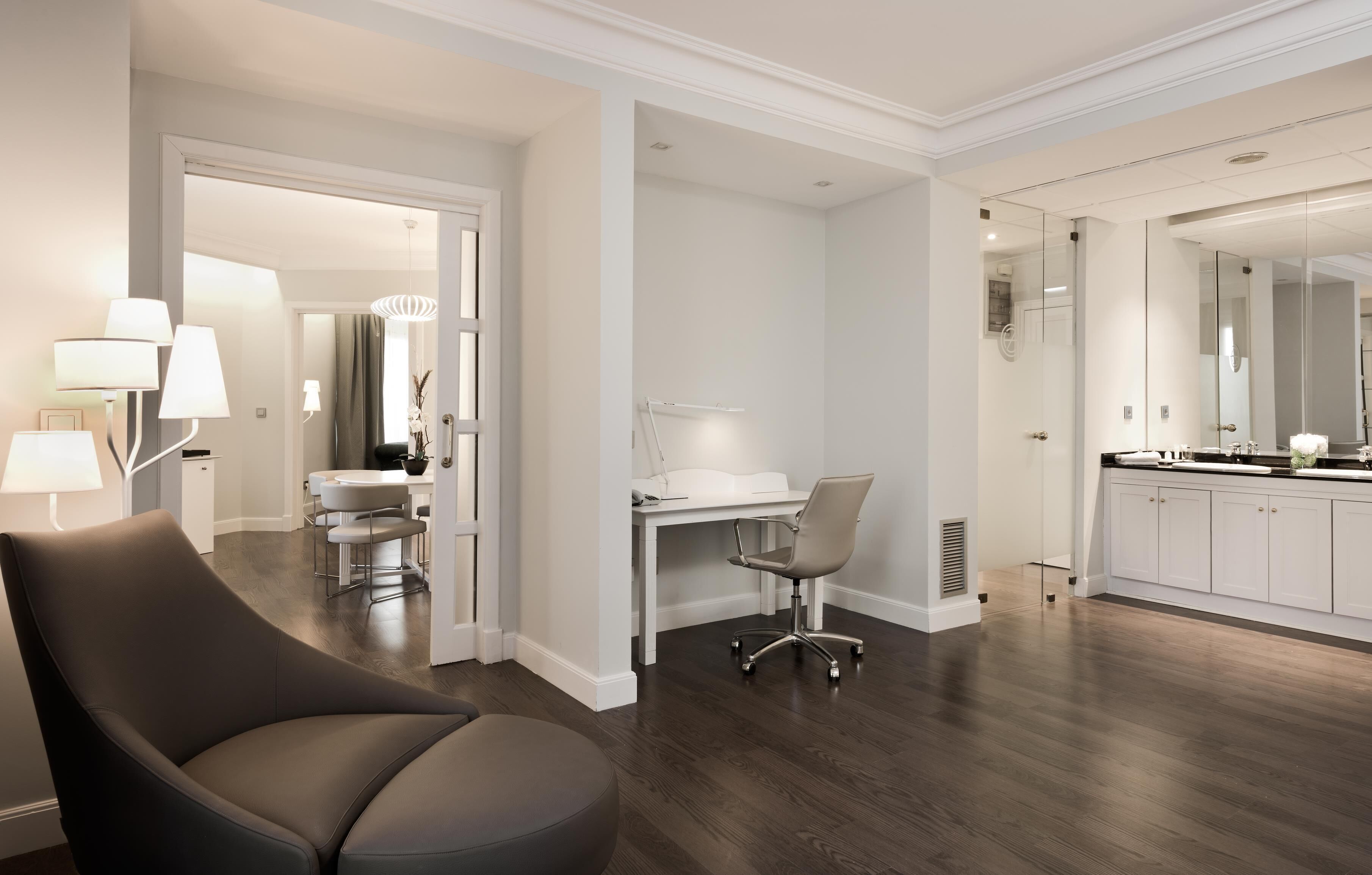 Una habitación moderna y bien iluminada con una silla curvada, un escritorio y un espejo grande.