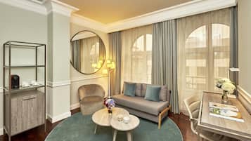 A modern hotel room with a sofa, two armchairs, a round coffee table, a small cabinet, and a dining table with a vase of flowers.