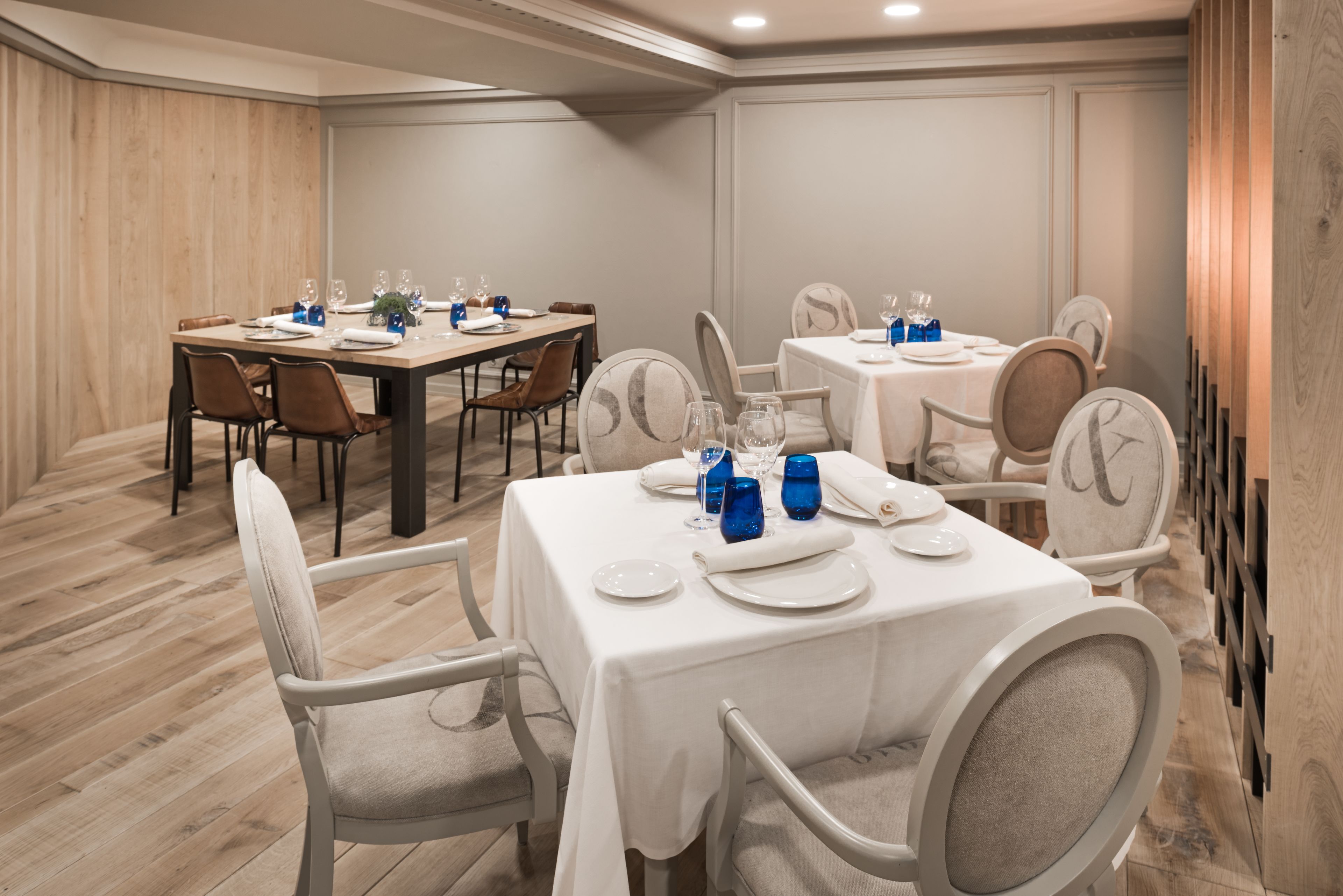 A dining area with tables set for four, each with white tablecloths, chairs, and blue glassware.
