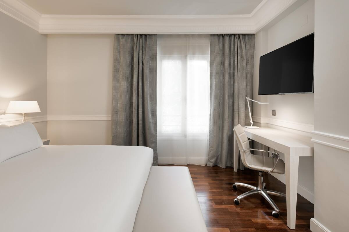 Habitación de hotel con cama, escritorio, silla y televisor en la pared.