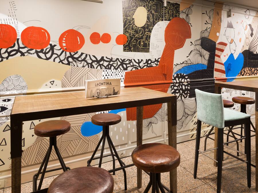 Una zona de bar con taburetes y una mesa, un menú sobre la mesa y una pared con arte abstracto.
