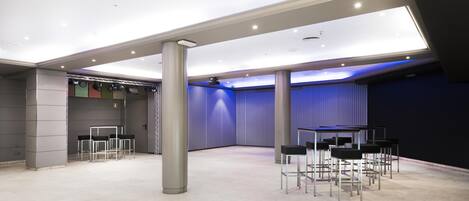 A spacious indoor area with high ceilings, modern lighting, and a stage with chairs.