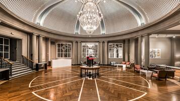 Un vestíbulo amplio y elegantemente diseñado, con un alto techo, una lámpara central y suelo de parquet.