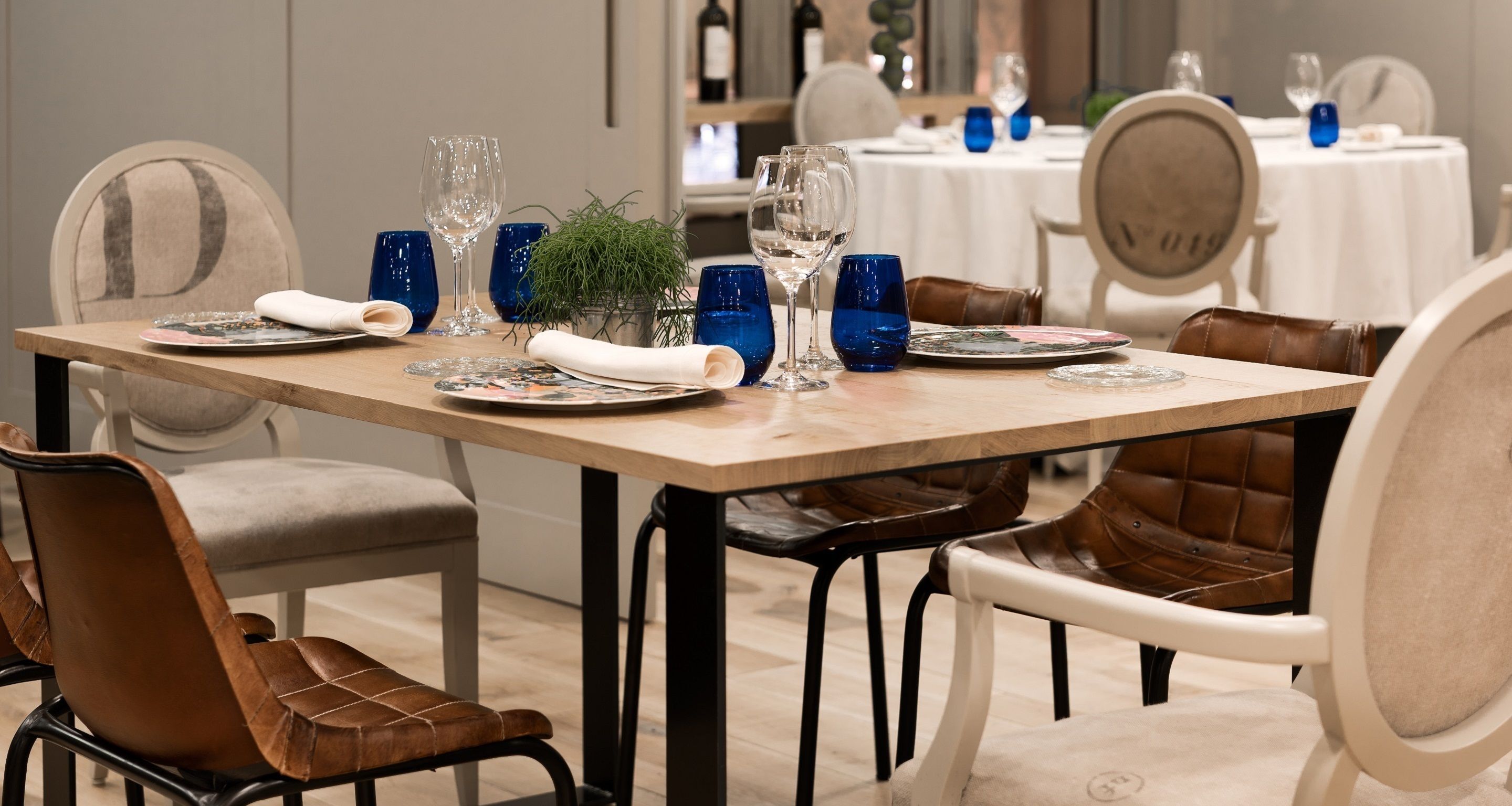 A dining table set with blue glassware, plates, and a small plant centerpiece.