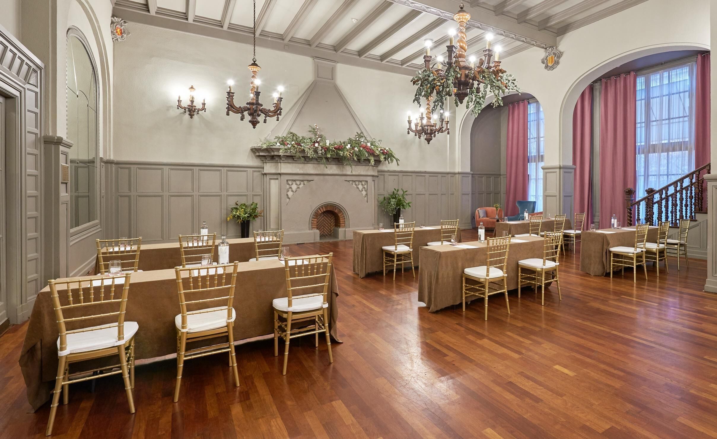Un amplio salón con suelo de madera, varias mesas con sillas y una chimenea con adornos florales.