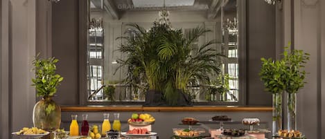A buffet setup with various food items and drinks, a chandelier, and potted plants.