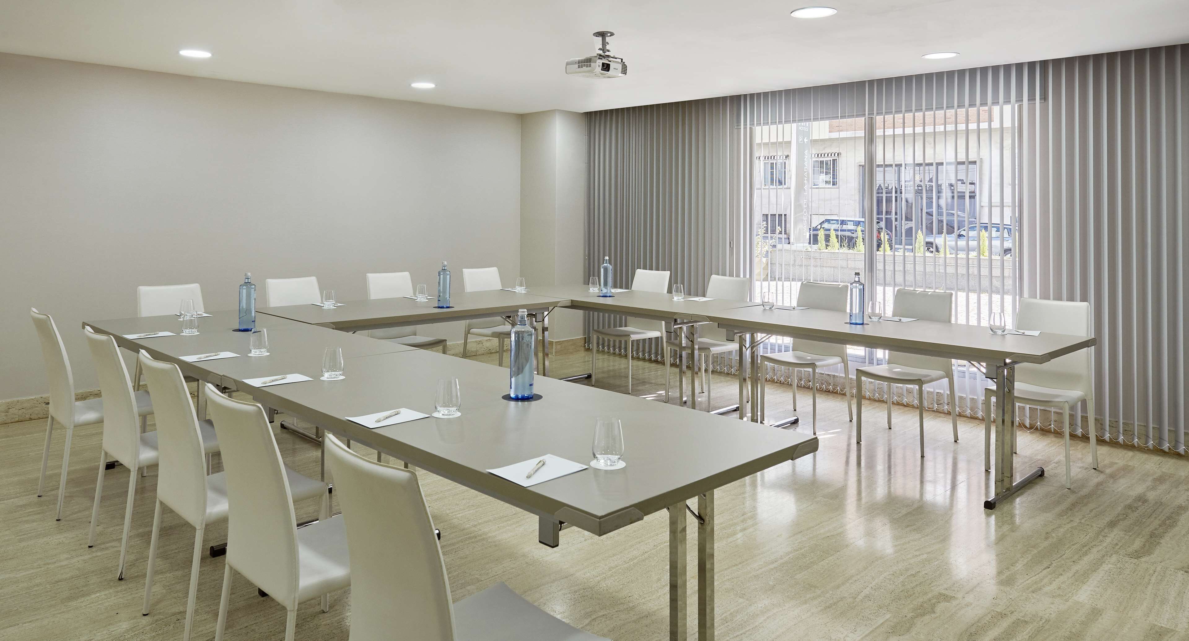 Un salón de conferencias con una larga mesa, sillas blancas y un proyector.