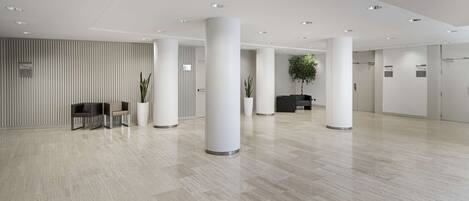 A spacious lobby with a modern design, featuring a light-colored floor, white columns, and a seating area with a plant.