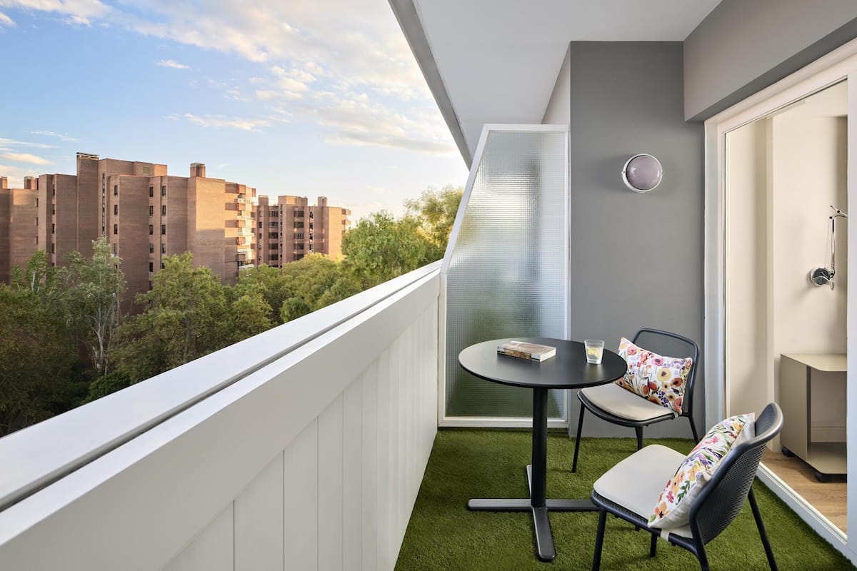 Un balcón con una mesita y sillas, vistas a edificios, y una puerta con perchero para toallas.
