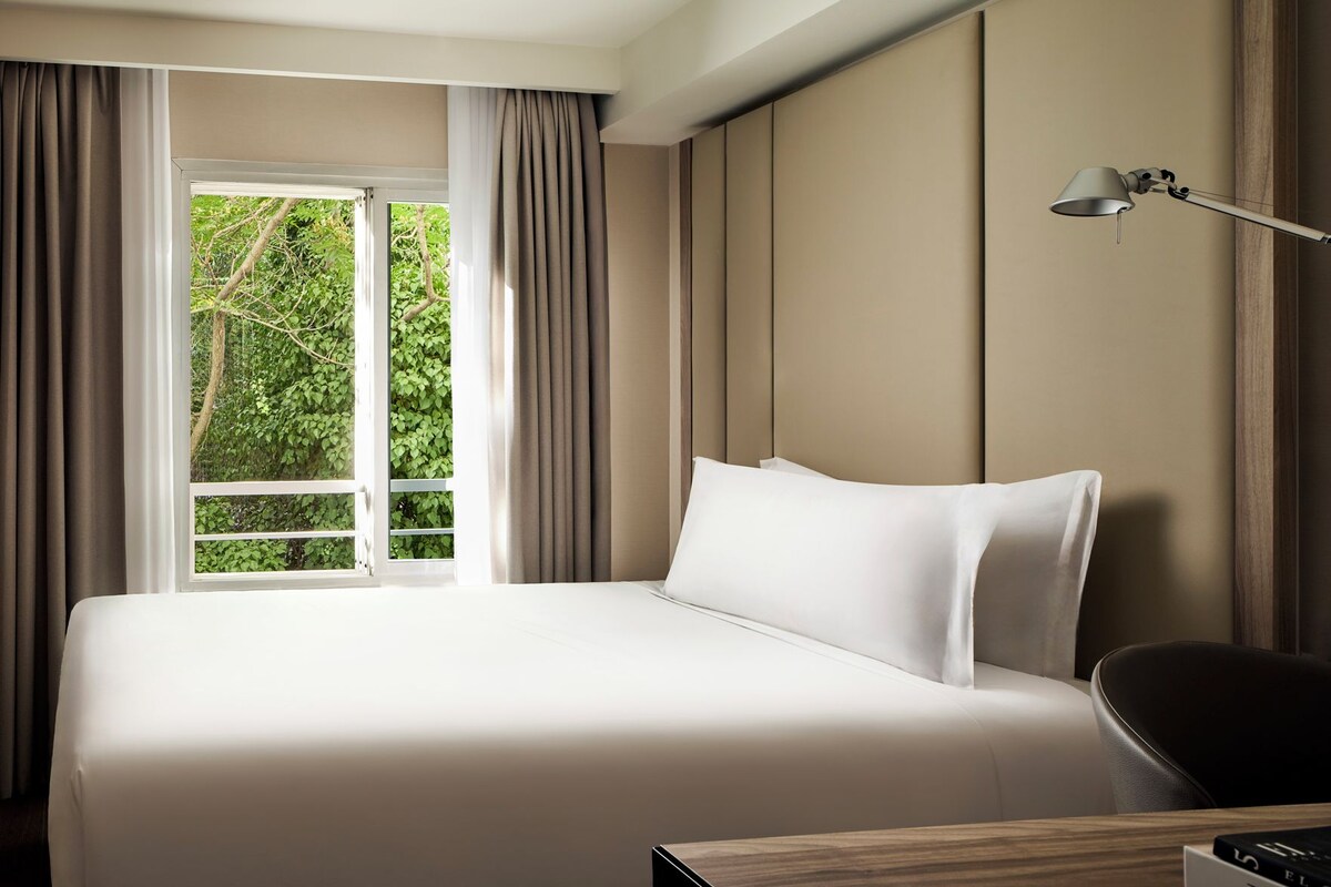 A hotel room with a bed, a desk, a lamp, and a window with curtains.