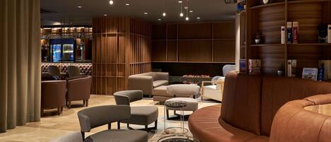 A modern lounge area with leather sofas, a bar, and a bookshelf with travel books.