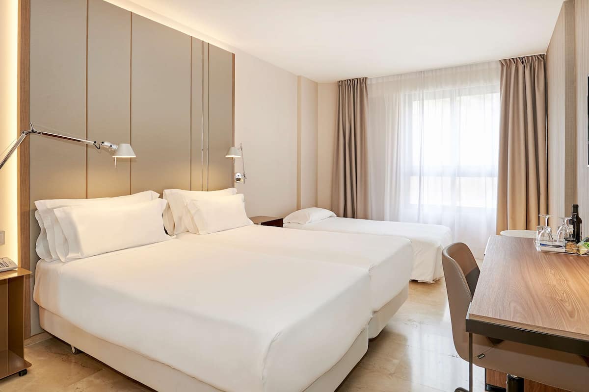 A hotel room with two beds, a desk, a chair, a TV, and a phone on the nightstand.