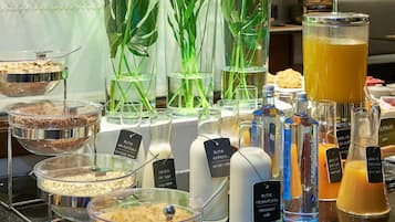 Un bufé con diversos alimentos y bebidas, que incluye una bebida de soya y jugo de melocotón.