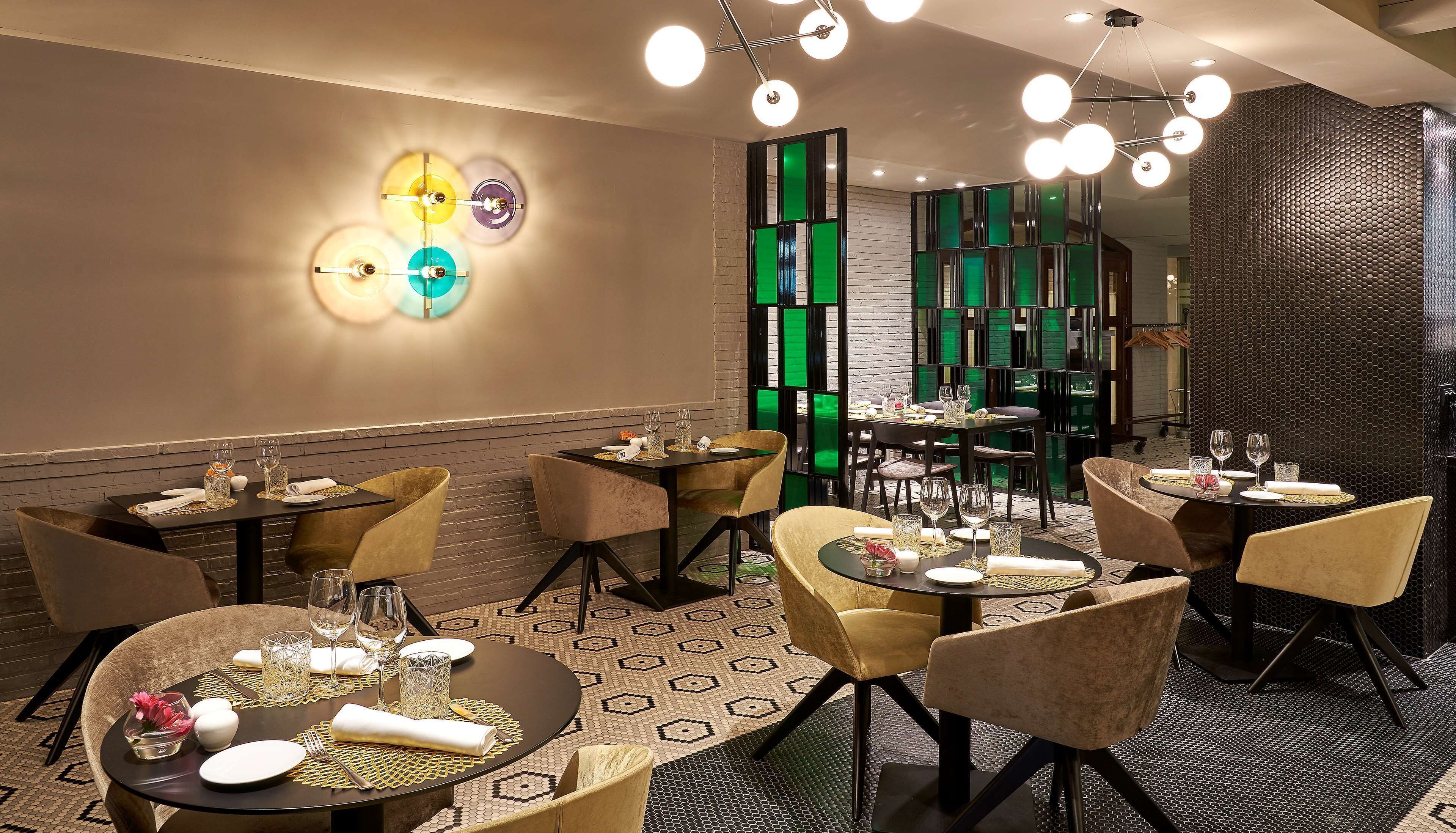 A restaurant with multiple tables set for dining, featuring a modern interior with geometric patterns on the floor and walls, and a variety of seating options.