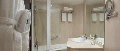 Un baño moderno con ducha envuelta en vidrio, un lavamanos con espejo y un perchero para toallas.