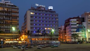 Un hotel con varios pisos, balcones y una zona de playa con barcos.