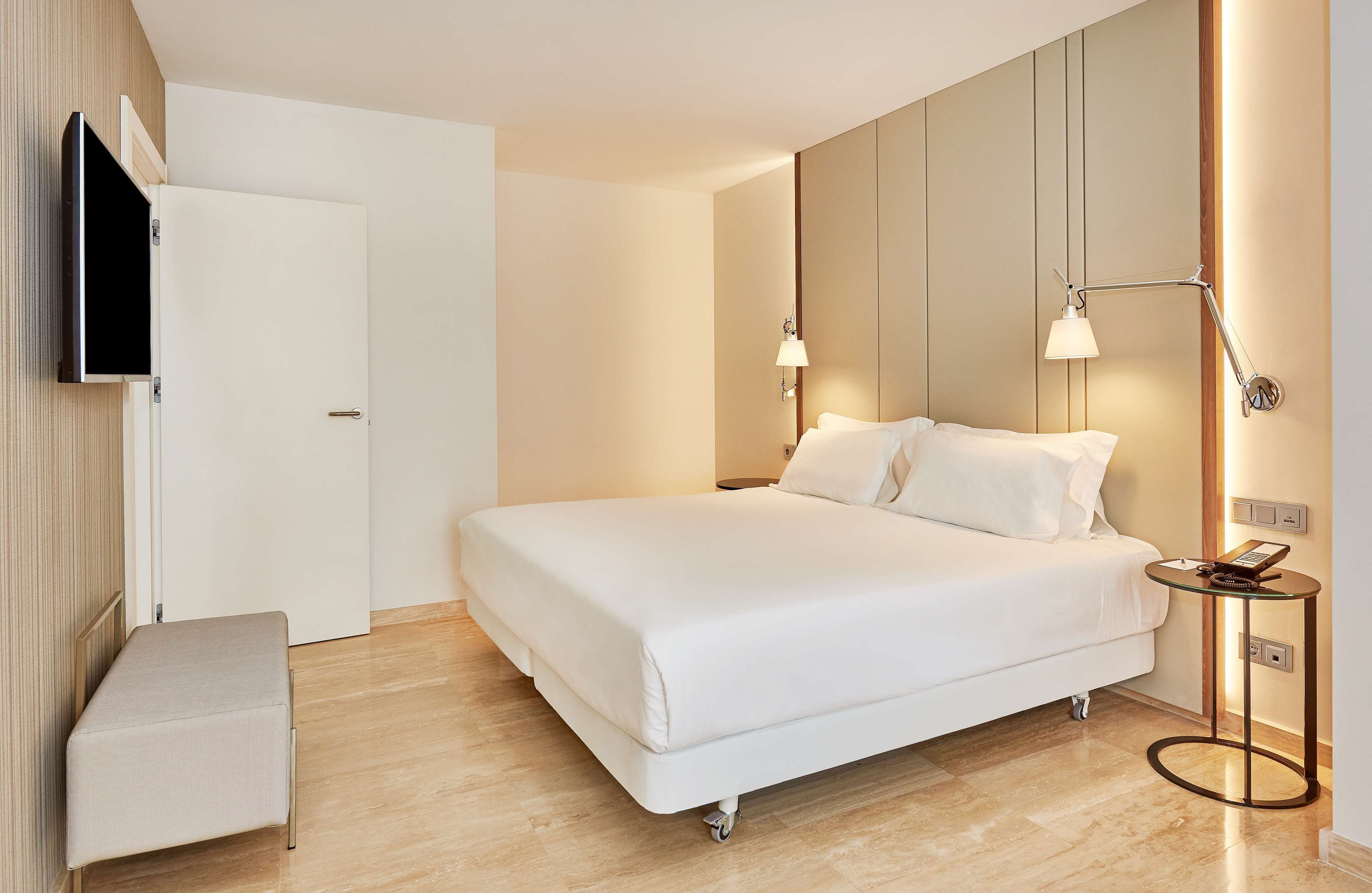 Ein modernes Hotelzimmer mit einem großen Bett, Nachttischen, einem Flachbildfernseher und einer Wandlampe.