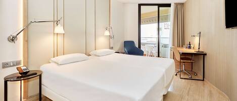 Une chambre d’hôtel avec un grand lit, des lampes de chevet, un bureau avec une chaise et une vue sur la façade de l’hôtel.