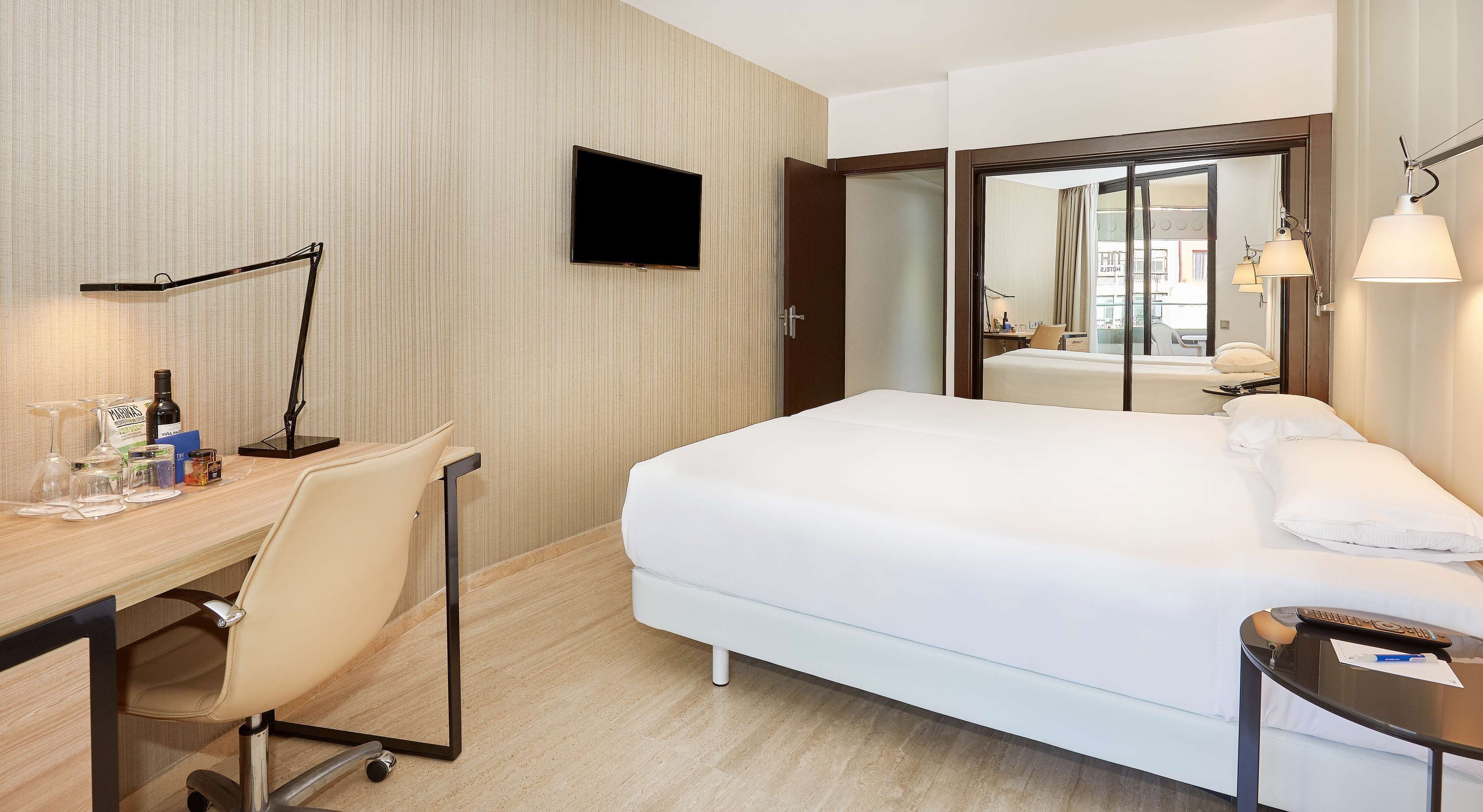 A hotel room with a bed, desk, chair, and a TV on the wall.