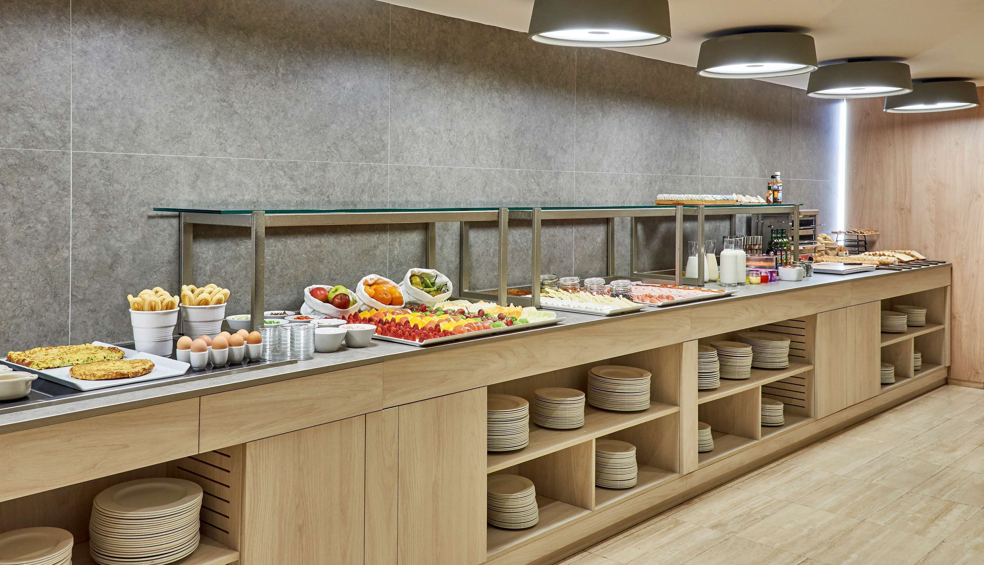 Tarjolla on runsas buffet, jossa on monenlaista ruokaa ja tarjoiluastioita, kuten hedelmiä, leivonnaisia ja juomia.