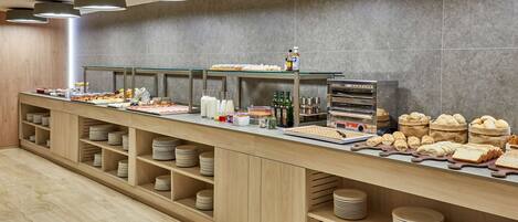 Montaje de bufé con diversos alimentos, bebidas y un horno para pan.