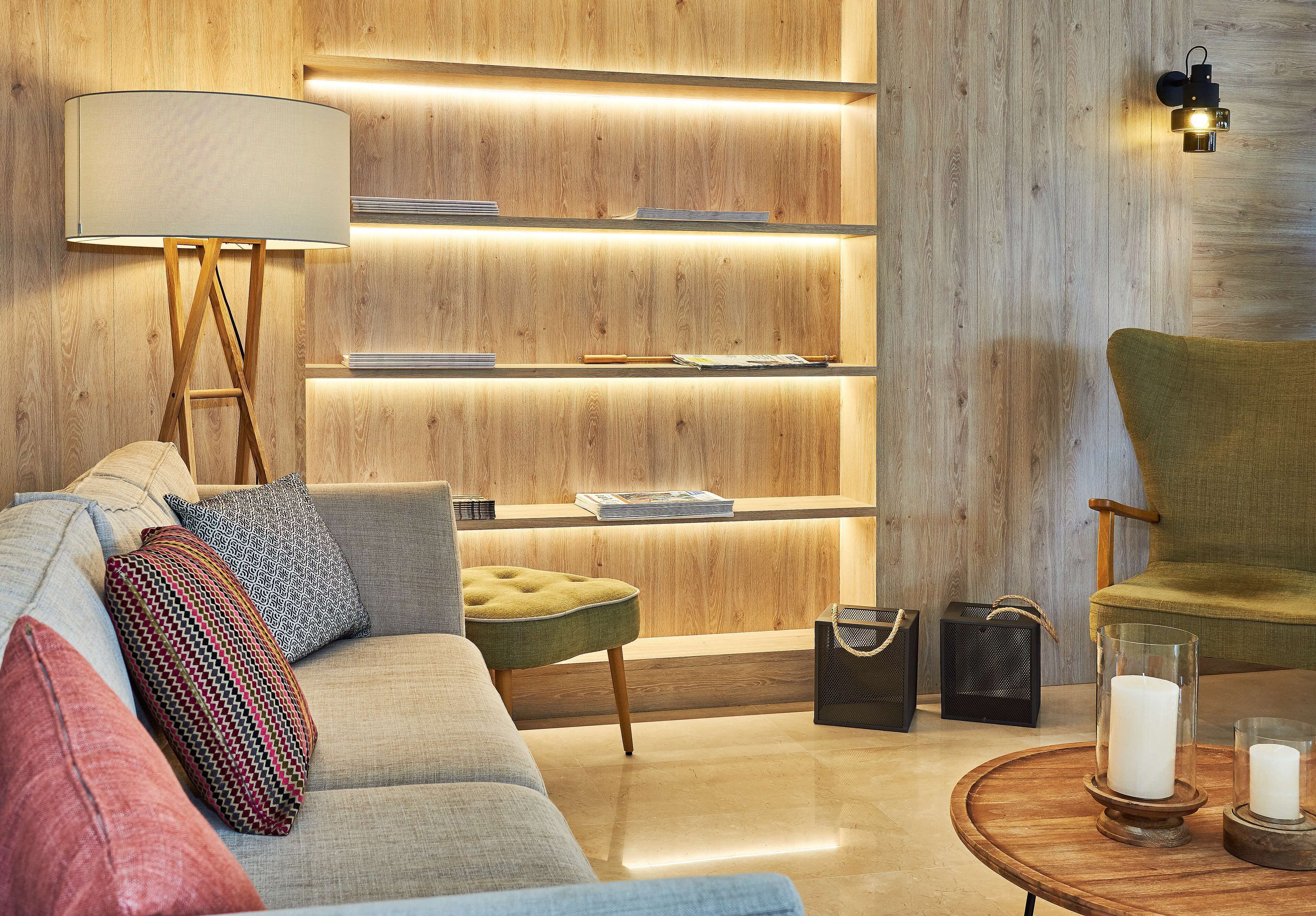A modern living room with a wooden wall, a sofa, a green armchair, a lamp, and a side table with candles.