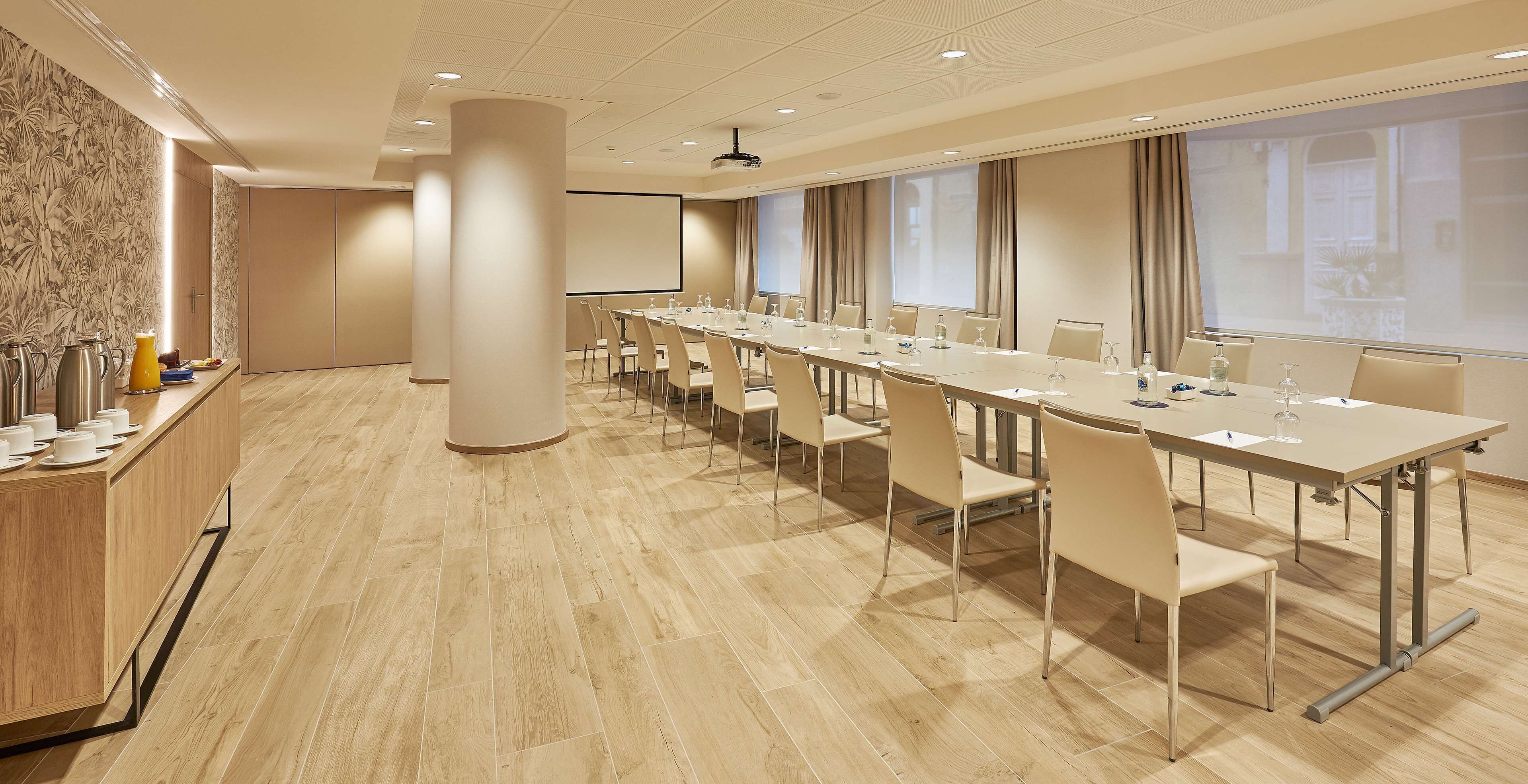Een vergaderruimte met een lange tafel, stoelen, een projectiescherm en een groot raam.