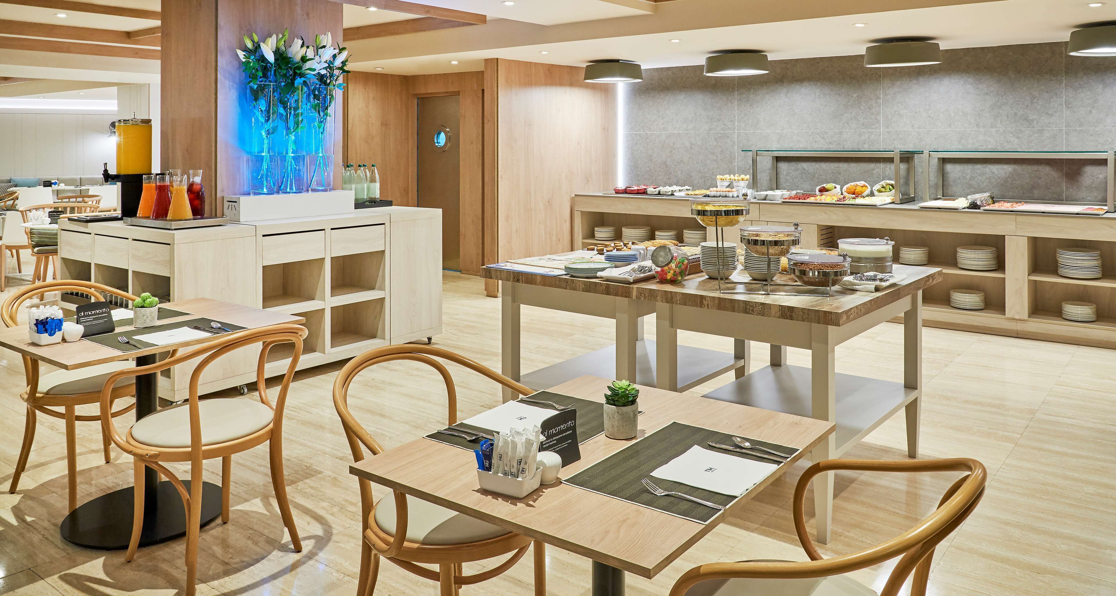 Een moderne eetruimte met houten tafels en stoelen, een buffet met diverse gerechten en een decoratieve wand met blauw licht.