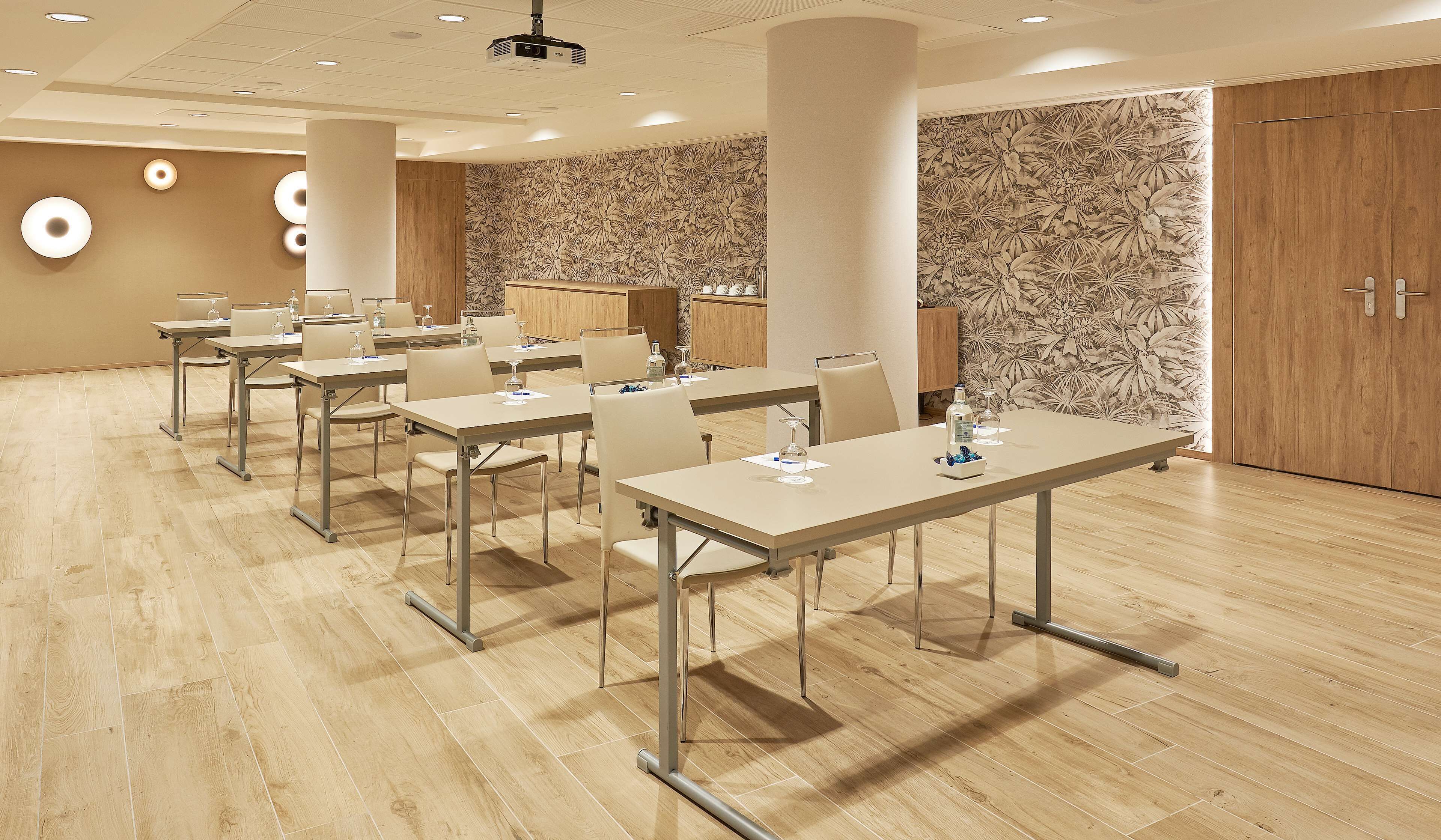 A conference room with multiple tables and chairs, a wooden floor, and a floral wallpaper on one wall.