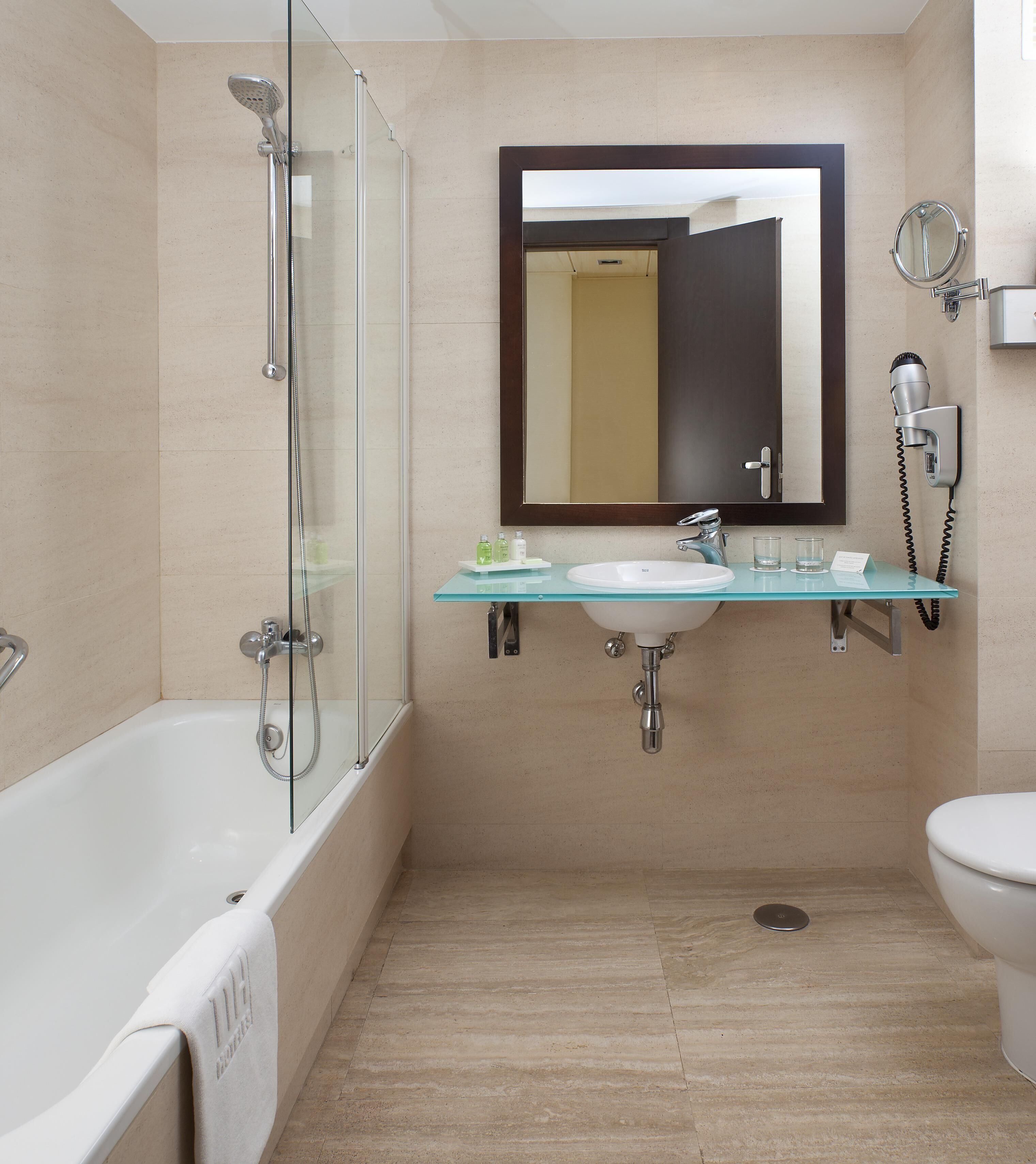 A modern bathroom with a glass-enclosed shower, a glass sink, and a toilet.