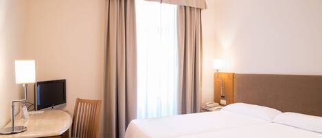 Una habitación de hotel con cama, escritorio con computadora, silla, teléfono y cortinas.
