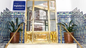 Entrada de un hotel con un cartel que dice "Hotel Inlatierra", puerta de vidrio, paredes con azulejos y dos plantas en macetas.