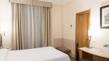 A hotel room with a bed, a desk, a chair, a small table, and a door.