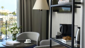 Et moderne hotelværelse med et glasbord, en sofa, en lampe, en kaffemaskine og udsigt over byen.