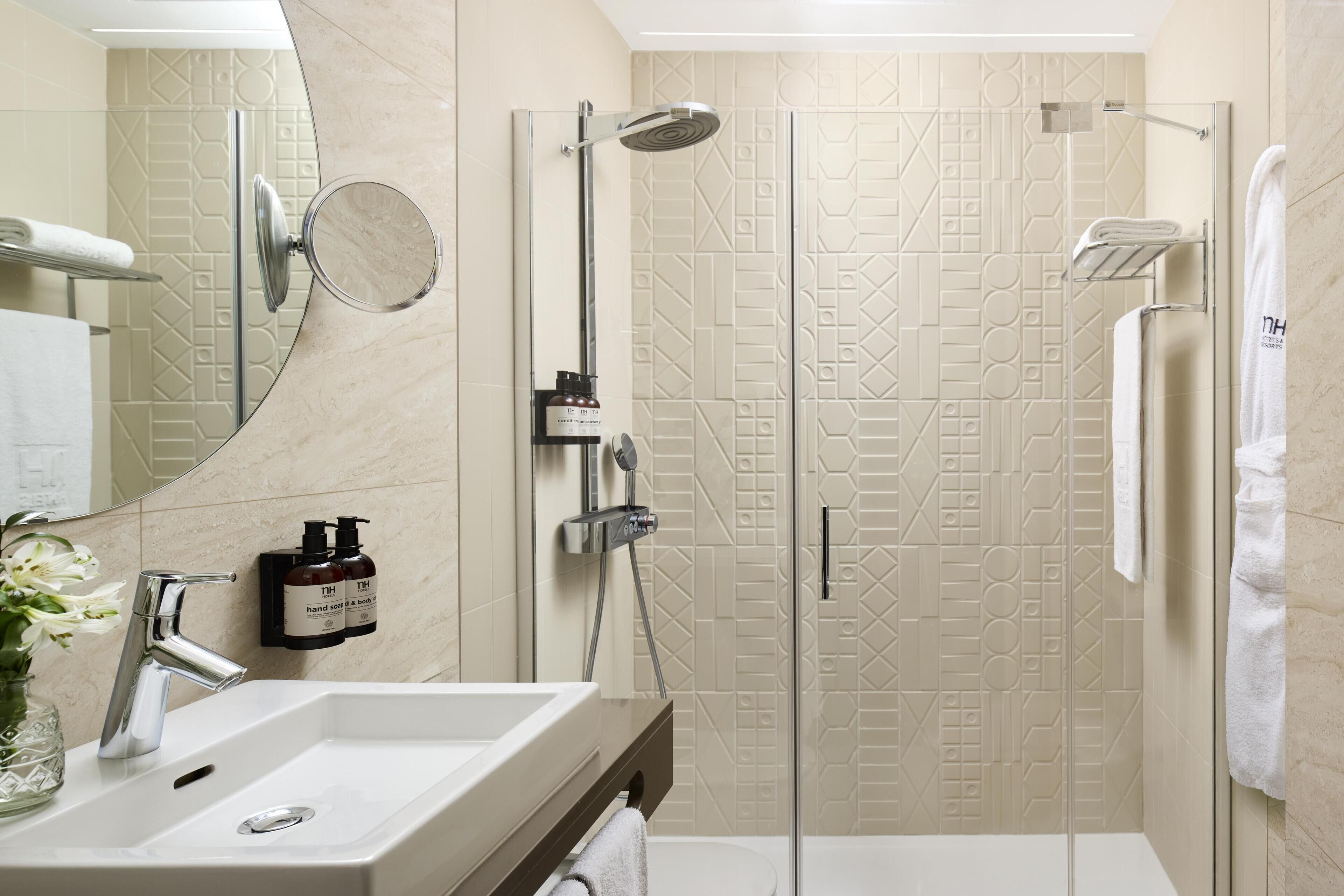 A modern bathroom with a large mirror, a sink, a shower with a glass door, and a towel rack.