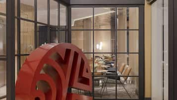 A modern interior with a large red sculpture, a patterned ceiling, and a dining area visible through glass doors.