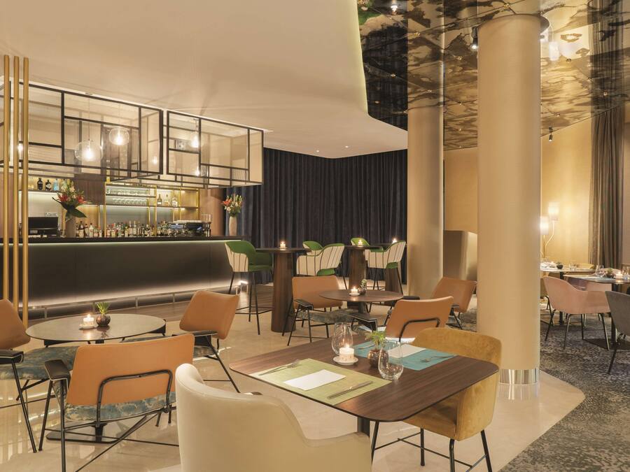 Un moderno vestíbulo de hotel con zona de bar, mesas redondas y asientos cómodos.