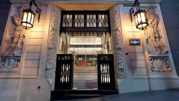 L’entrée de l’hôtel JOUSTEN se distingue par ses détails architecturaux raffinés, ses deux lanternes illuminées et une enseigne placée au-dessus de la porte.
