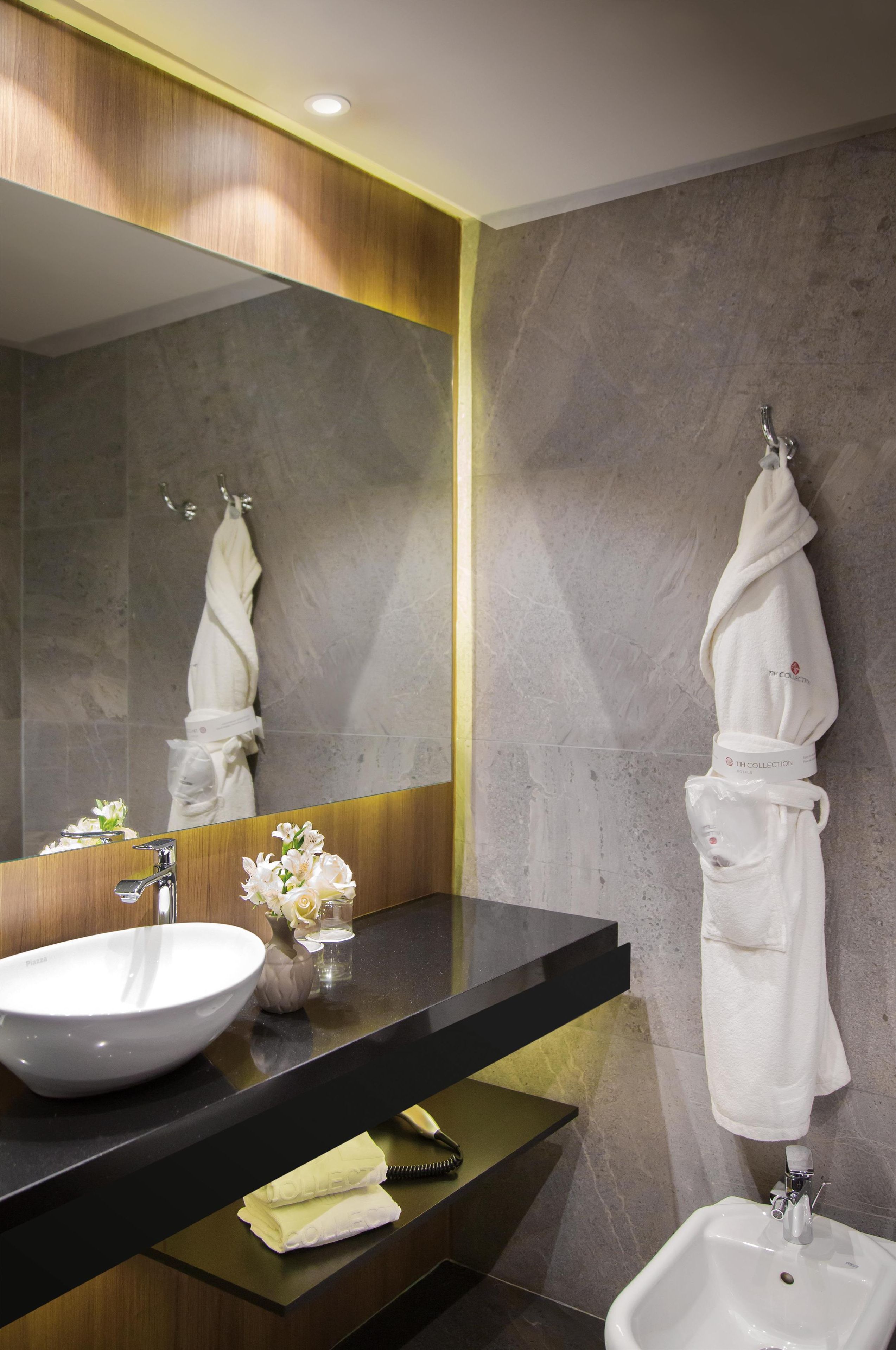 A modern bathroom with a large mirror, a white sink, a bidet, and a towel rack.