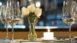 Une table dressée avec des verres à vin, une bougie et un vase contenant des roses blanches.