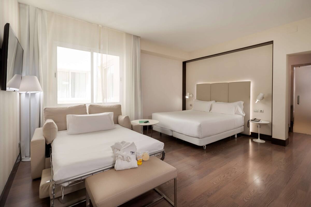 A hotel room with two beds, a sofa, a small table, and a bench.