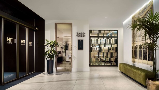 A hotel lobby with a modern design, featuring a reception desk, a seating area, and a large window with a view of the outside. - NH Madrid Lagasca (Madrid)