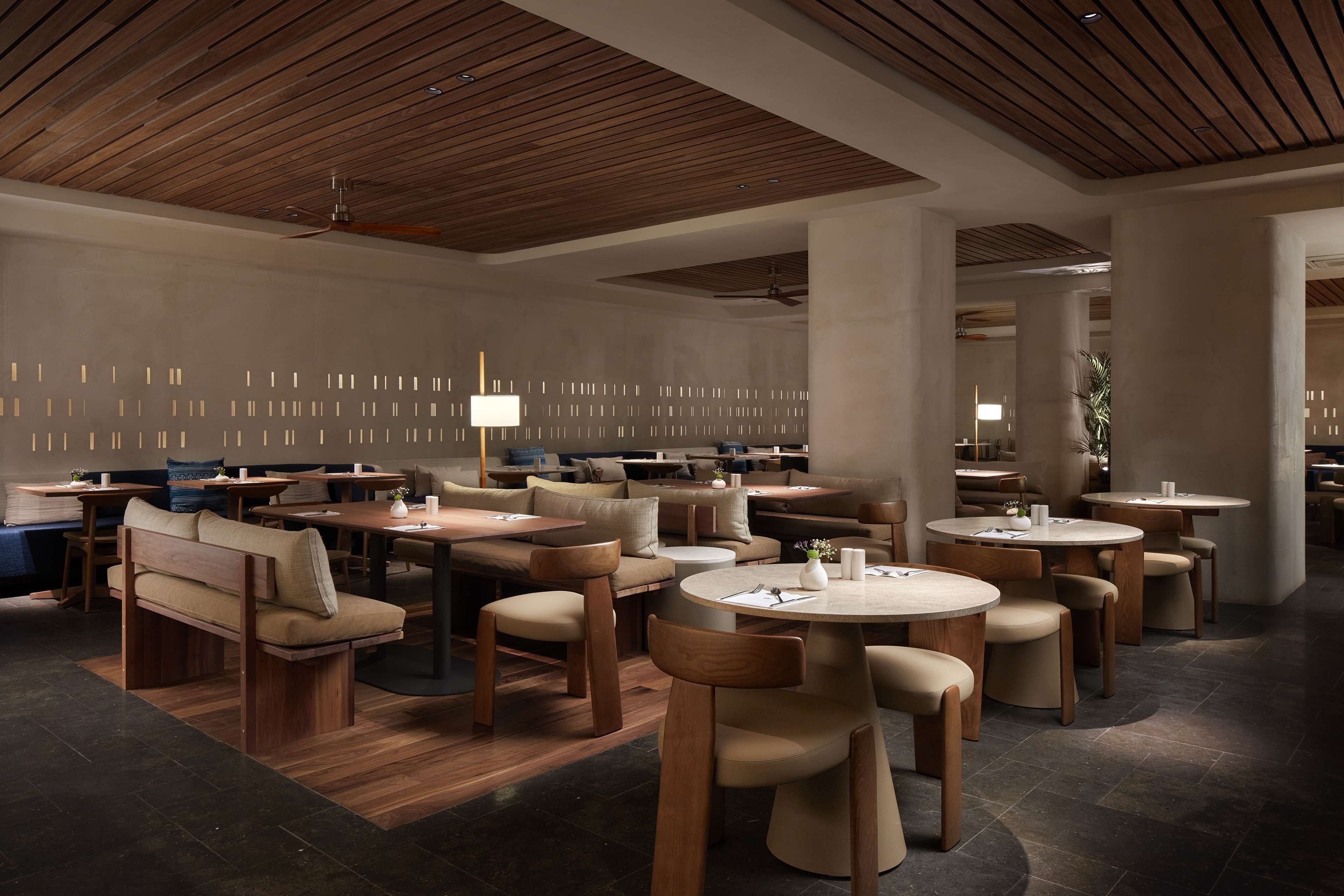 Un restaurante moderno con muebles de madera, mesas redondas y un techo con vigas de madera.
